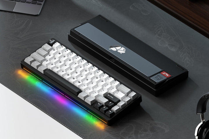 Mechanical keyboard with RGB lighting on a desk with a laptop and gaming accessories.